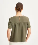 Blusa de poliéster color verde oliva, con cuello redondo, manga corta y detalle de pliegues fruncidos en la costura de los hombros.