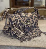 Mini bag bandolera de cuero con estampado animal print de leopardo, decorada con flecos largos en el frente y una hebilla metálica frontal ajustable. Cuenta con correa regulable y herrajes en tono bronce envejecido.