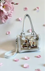 Cartera de cuero natural de diseño contemporáneo y versátil, intervenida con arte original por Carolina De Cunto en el frente, combinando tonos marfil y arena con detalles pintados a mano. Cuenta con estructura firme, herrajes de metal, manijas superiores, correa regulable desmontable y bolsillos internos y externos.