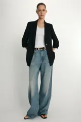 Blazer negro con cuello solapa con muescas, hombreras y forro interior a tono. Presenta manga por debajo del codo con detalle de drapeado y falsos bolsillos de vivo en el delantero, con cierre frontal de un solo botón dorado.