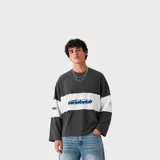 Remera manga larga de corte oversize, color gris oscuro con una franja blanca horizontal en el centro y las mangas. Cuenta con estampado tipográfico azul en el pecho.