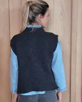 Chaleco de punto gris oscuro con diseño de trenzas y rombos en relieve, cuello redondo y terminaciones acanaladas.