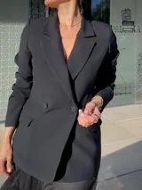 Blazer negro de corte sastre, con solapas clásicas, cierre frontal de doble botonadura y bolsillos laterales con solapa.