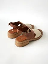 Sandalias de cuero combinadas en color marrón y crudo, con suela track y taco bajo. Tienen tira ajustable con hebilla en el talón.
