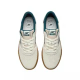 Championes New Balance modelo 272, con diseño de perfil bajo en color crema y detalles en verde petróleo. Presentan una suela de goma color caramelo, cuerpo de lona y gamuza, y el logo característico de la marca en los laterales.