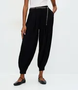 Pantalón de sastrería modelo aladim, color negro, confeccionado en crepé. Presenta pliegues en la cintura, corte holgado con piernas anchas que se estrechan en los tobillos y detalle de cinturón de cadena metálica.