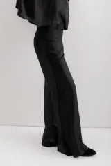 Pantalón de pierna ancha con acabado brillante, confeccionado en lino. Presenta un diseño de tiro medio con cierre de botón y cremallera, bolsillos traseros y etiqueta de marca en la cintura.