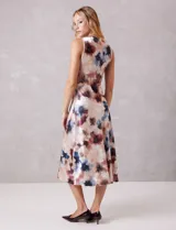 Vestido midi de satén fluido con estampado floral en tonos beige, azul y borravino. Presenta cuello volcado, diseño sin mangas y un drapeado lateral fruncido en la cintura que aporta movimiento a la falda de corte evasé.