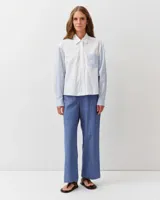 Camisa de algodón con diseño combinado. El cuerpo es de color blanco liso, mientras que las mangas largas y el bolsillo frontal aplicado presentan un patrón de rayas finas celestes y blancas. Cuenta con cuello clásico y cierre frontal de botones.