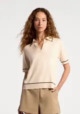 Polo de manga corta en tejido de punto color beige, con cuello tipo polo y detalles de líneas finas en color negro en el cuello, mangas y ruedo.
