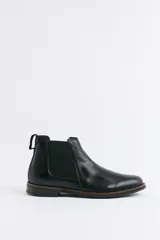 Bota tipo Chelsea de cuero negro con paneles elásticos laterales, suela de goma con detalle de vira en contraste y tirador trasero.