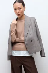 Sweater de punto color beige con cuello redondo y mangas largas, combinado con una camisa blanca de cuello y botones que sobresale por debajo.