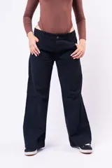 Pantalón wide leg de tiro bajo en color negro, confeccionado en denim, con cierre frontal de botón y bolsillos laterales.