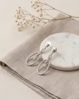Caravanas colgantes con baño de rodio, diseño de óvalo con pavé de cristales y un cristal central facetado.