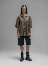 Camisa de manga corta color verde militar, con cuello clásico y cierre de botones frontales. Presenta un estampado floral en relieve.