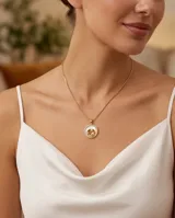 Collar de cadena dorada con dije circular de bronce que presenta una figura de madre e hijo en relieve sobre fondo de nácar, bordeado por incrustaciones de circonia.