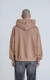 Hoodie oversize color marrón, confeccionado en algodón rústico. Presenta capucha forrada, bolsillo frontal tipo canguro y un bolsillo utilitario con cierre en la manga izquierda, con detalles en microfibra.