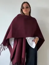 Ruana de tejido suave en color bordó, con diseño amplio y terminaciones con flecos en los bordes.