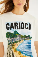 Remera blanca de manga corta y cuello redondo, con estampa frontal ilustrada de un paisaje de playa con la inscripción "Carioca".