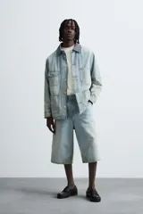 Bermudas de denim de algodón, color celeste claro con efecto lavado y manchas marrones/beige en las perneras. Tienen un corte ancho (baggy fit) y terminación de bajo irregular.