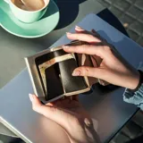 Billetera tarjetero automática con estructura de aluminio y revestimiento de cuero bicolor en tonos verde oliva y beige. Cuenta con un cierre de broche a presión y el logo de la marca grabado en la parte inferior.