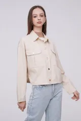 Chaqueta de algodón color beige, con diseño holgado, cuello tipo camisa, cierre frontal con botones metálicos y bolsillos frontales con solapa.