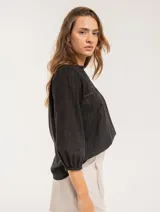 Blusa blanca de algodón con escote redondo, manga tres cuartos y silueta oversized. Presenta bordados y texturas combinadas.