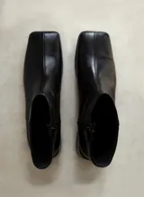 Bota corta de cuero negro con punta cuadrada y costura central vertical. Cuenta con cierre lateral interno.