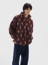 Campera de sherpa con estampado de rombos en tonos bordó, naranja y rosa. Presenta cuello alto, cierre frontal parcial con tirador naranja a contratono y bolsillos laterales.