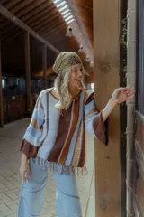 Sweater tejido en hilado 100% algodón con diseño a rayas verticales en tonos rojo, blanco, marrón y negro. Presenta flecos en el ruedo y bordados en el escote.