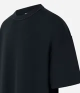 Remera negra de algodón con corte oversized, cuello redondo y manga corta. Presenta un tejido acanalado y un dobladillo sin rematar.