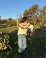 Sweater tejido a mano en mohair, de cuello redondo y manga larga. Presenta un diseño de canesú con patrón geométrico en tonos amarillo y blanco sobre una base de color marrón.