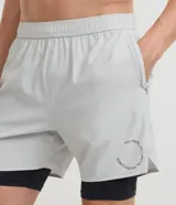 Bermuda deportiva verde militar con short de compresión incorporado, cintura elástica y cordón ajustable, confeccionada en microfibra de poliéster y elastano.