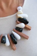 Collar de diseño artesanal compuesto por piezas de resina en forma de gotas y cilindros alargados en tonos blanco, negro y marrón, montadas sobre un cordón de hilo encerado.