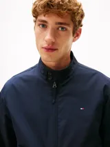 Campera tipo Harrington de Tommy Hilfiger en color azul marino, de corte amplio. Cuenta con cuello alto, cierre frontal de cremallera, bolsillos de ojal en la cintura y el pecho con el logo bordado.