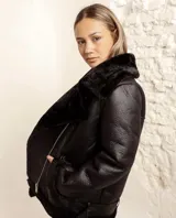 Campera tipo gamulán de cuero vegano negro con interior y cuello de piel sintética al tono. Presenta cierre frontal cruzado y diseño de corte clásico.
