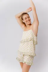 Pijama de algodón estampado con lunares dorados sobre fondo crema. Incluye una musculosa con tirantes finos y volados en el pecho, y un short con elástico en la cintura y volados en el ruedo. Los volados presentan un estampado floral en tonos verdes y crema.