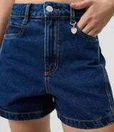 Short de jean azul oscuro con corte evasé, bolsillos delanteros y traseros, pasacintos en la cintura y cierre frontal con botón y cremallera. Incluye un pequeño aplique metálico de corazón.