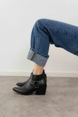 Botas cortas de cuero negro con puntera fina, caña baja con elásticos laterales y hebilla decorativa.