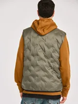 Chaleco acolchado de peso medio en color gris, con cierre frontal completo y parche de silicona con logo de la marca en el pecho. Cuenta con bolsillos laterales tipo welt y ribete elástico en el dobladillo.