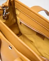 Cartera mediana de símil cuero color habano, con doble asa corta de mano y correa ajustable extraíble. Cuenta con un bolsillo frontal con broche a presión, herrajes metálicos plateados y un llavero colgante en forma de corazón.