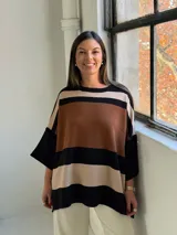 Poncho de tejido de punto con diseño de rayas horizontales anchas en tonos negro, marrón y beige, con cuello redondo y mangas amplias.
