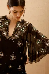 Vestido corto negro de tela transparente con mangas acampanadas y escote en V. Está completamente bordado con motivos florales y estrellas en lentejuelas y cuentas plateadas y verdes.