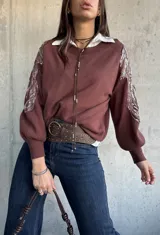 Sweater de punto color chocolate con cuello redondo y mangas largas abullonadas. Presenta detalles bordados con lentejuelas brillantes en los hombros y parte superior de las mangas.
