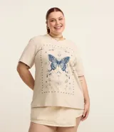 Remera color beige de corte alargado, cuello redondo y mangas cortas. Estampado frontal con una mariposa azul rodeada de elementos celestiales.