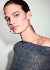 Top de encaje gris oscuro con diseño semitransparente, cuello asimétrico de hombro descubierto y manga larga.