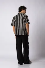 Camisa de manga corta tejida al crochet con diseño de rayas verticales negras sobre una base color crudo. Presenta cuello solapa y cierre frontal con botones.