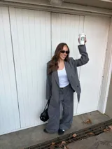 Conjunto de blazer y pantalón de lino gris con diseño de rayas diplomáticas. El blazer es de corte amplio con doble botonadura, y el pantalón es de corte recto y tiro alto.