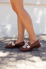 Zapato mocasín de cuero color marrón, con detalle de antifaz con aplique de cuero con estampado animal print y flecos.