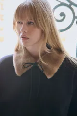 Buzo negro de felpa con interior suave, cuello de piel sintética en color marrón, mangas largas con hombros caídos y puños y bajo acanalados. Presenta tiras finas para atar en el frente.